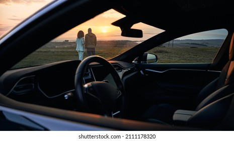 Back View Of Young Couple In Love Enjoying Sunset Automobile Date At Nature Environment, Husband And Wife Spending Evening For Bonding Togetherness With Black Car For Trip Travelling On Front