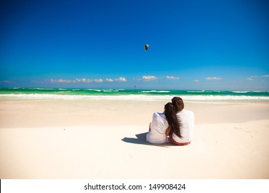 Back view of young couple sitting at tropical white beach