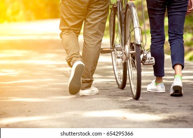 Back view of young couple walking  together with bicycle in the garden in vintage color tone