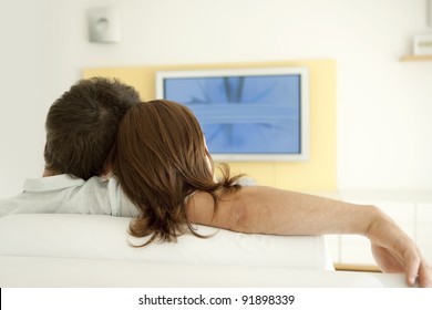 Back View Of A Young Couple Watching Tv At Home, Relaxing.