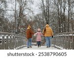 Back view of young family with child walking on bridge together and holding hands enjoying day in winter park copy space