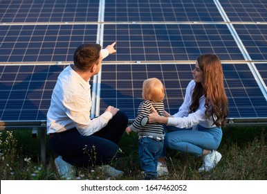 Back View Of Young Family Of Three Crouching Near Photovoltaic Solar Panel, Getting Acquainted With Alternative Energy, Modern Family Concept