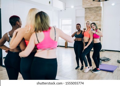 Back View Of Young Female Blogger Wearing Sports Bra And Trendy Leggings Taking Mirror Selfie With Friends After Group Fitness Class In Studio