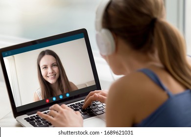 Back view of young female in headset talk on video call on laptop with smiling friend or sister, woman in earphones enjoy online webcam communication on computer with happy girl colleague at home - Shutterstock ID 1689621031