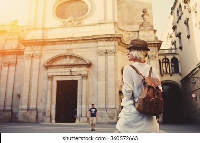 Back View Of A Young Female Wanderer Out Sightseeing In A Foreign City During Weekend Overseas, Trendy Woman Traveler With A Rucksack On Her Back Walking On Unfamiliar Street During Summer Adventure 