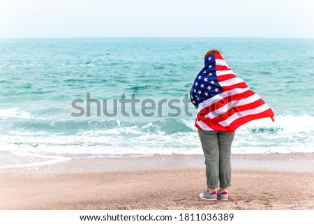 Back view of young girl with an American flag looks at the sea. America flag holiday concept