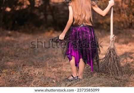 Back view of a young girl with long dark hair dressed as a witch with a broom. Walk through the autumn forest on Halloween Eve. Disgusting or sweet. Background, copy space, space for text. Costume