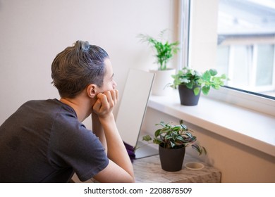 Back View. Young Guy With Applied Hair Dye Sitting In Front Of Mirror And Looking At Window Thinking. Beauty Salon At Home Concept. The Process Of Hair Coloring, Man Gets New Hair Color.