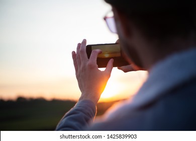 
Back view of young guy take pictures of sunset by smartphone