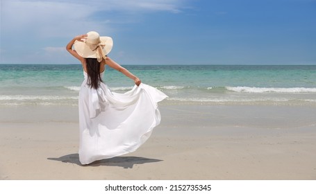 Back view young happiness asian traveller woman in white dress and hat standing on beautiful sandy beach. Cute girl enjoy her tropical sea on relax holiday vacation during summer time and sunshine day - Powered by Shutterstock