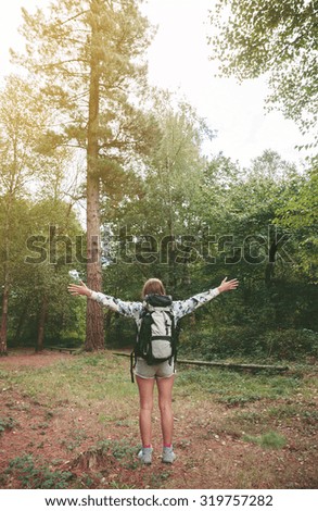 Hiker woman with backpack raising her arms into the forest