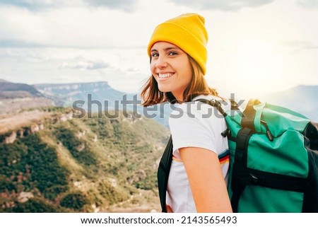 Back view young happy smiling woman backpacker with brunette hair relaxation on top rocky mountains, with backpack, yellow hat. Leisure after walking valley. Adventure, travel, holiday concept.