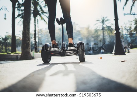 Back view of young hipster girl balancing on electric hoverboard at the sunny park, active woman using and driving on segway outdoor, film effects, flare light