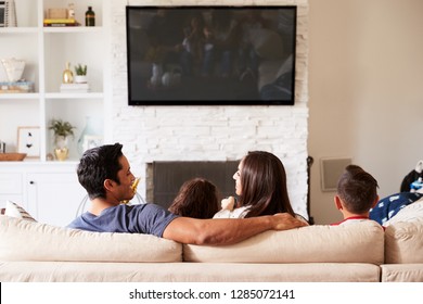 Back View Of Young Hispanic Family Of Four Sitting On The Sofa Watching TV, Mum Looking At Dad