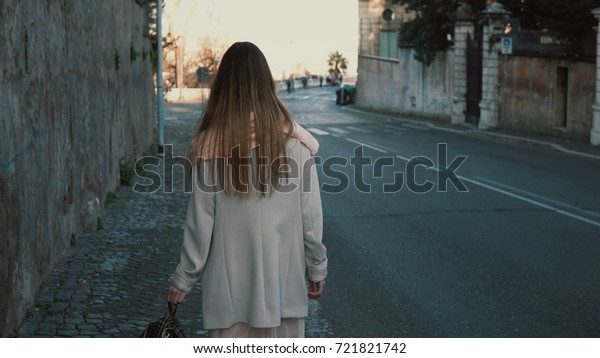 Back\
view of young lady walking in the city centre alone. Female with\
long hair going near the road, enjoying the\
day.