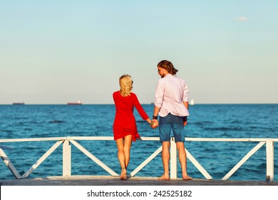 Back view of young lovely couple standing on the pier and waiting  their  yacht . Evening warm light.