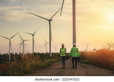Back view of young maintenance engineers team working in wind turbine farm at sunset. - Shutterstock ID 2210747321
