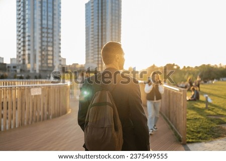 Back view of young man with backpack standing on wooden bridge and looking at city
