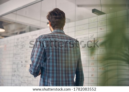 Back view of young man in checkered shirt looking at whiteboard at work
