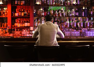 Back view of a young man drinking beer while while sitting at the bar counter - Powered by Shutterstock