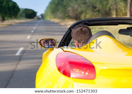 Back view of a young man driving his convertible yellow car. Open roof