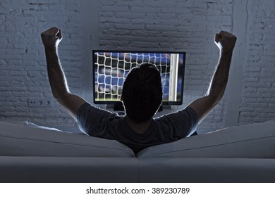 Back View Of Young Man Home Alone Watching Soccer Or Football Game In Television Enjoying And Celebrating Goal And Victory Gesturing With Fist Sitting On The Sofa Happy And Excited