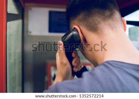Back view of young man making a call from public phone box
