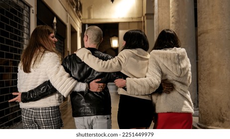 Back view of a young man is seen walking with three women in an alley. The group appears to be going home from a nightclub, and the young man looks like he is drunk with his arm around women. - Powered by Shutterstock