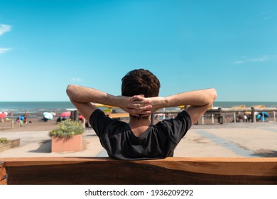 Back view of a young man sitting on a bench on the shore and enjoying the sunny day. - Powered by Shutterstock