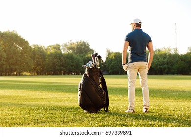 Back View Of A Young Man Standing On A Green Field With Golf Bag