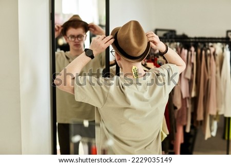 Back view of young man trying on hat in thrift store and looking in mirror, focus on sale tag, copy space