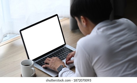 Back view of young man using laptop while lying on floor at home.