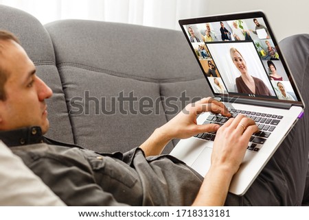 Back view of young man using headset and laptop and having videoconference at home