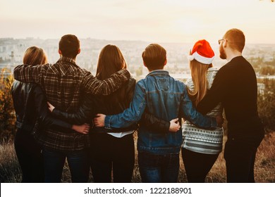 Back View Of Young Men And Women Hugging Each Other And Looking At Modern City While Celebrating Christmas Together.
Group Of Friends Celebrating Christmas Outside.