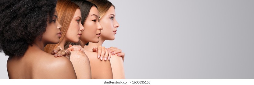 Back view of young multiracial female models standing in line and touching bare shoulders showing beautiful skin on light grey background