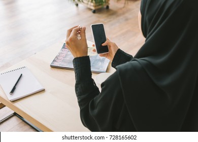 back view of young muslim woman using smartphone in cafe