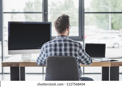 Back View Of Young Programmer Working With Laptop And Desktop Computer