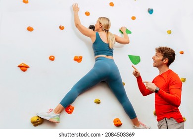 Back view of a young sporty woman climbing on practical wall at gym. Personal trainer giving instructions to her client. Bouldering centre. Healthy lifestyle, sport concept. - Powered by Shutterstock