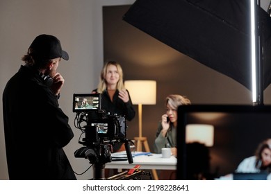 Back view of young videographer standing in front of steadicam during shooting of commercial with female model in studio