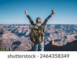 Back view of young wanderlust feeling victory conquering mountain in Grand Canyon, female traveler with backpack raising hands enjoying beautiful nature from high rocky hills getting to destination