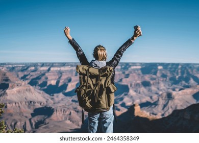 Back view of young wanderlust feeling victory conquering mountain in Grand Canyon, female traveler with backpack raising hands enjoying beautiful nature from high rocky hills getting to destination - Powered by Shutterstock