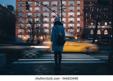 Back view of a young woman with backpack waiting for green traffic light while standing at the Chelsea district, New York City , USA