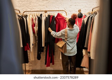 Back view at young woman browsing clothing racks in boutque or second hand shop, copy space - Powered by Shutterstock