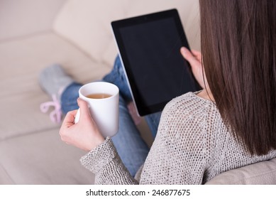 Back view of young woman is drinking a tea and using tablet at home. - Powered by Shutterstock