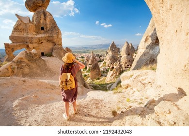 Back view of young woman exploring valley with rock formations and fairy chimneys near Uchisar castle in Cappadocia Turkey