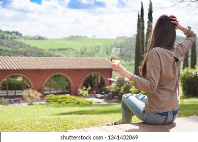 back view of young woman with glass of chilled white wine over Tuscany backgound