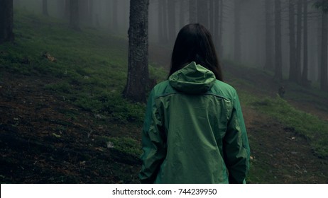 Back View Of A Young Woman Hiking In Forest. Hiking Woman Walking In Gloomy Mystical Forest - Thriller Scene. Wide-angle Lens. Close-up
