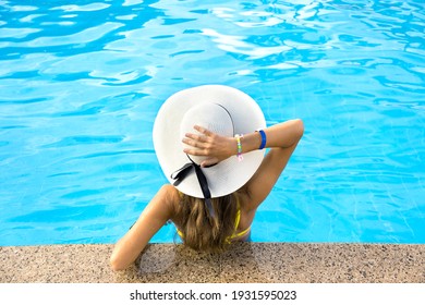 Zurück Blick auf junge Frau mit langes Haar mit gelbem Strohhut entspannen im warmen Sommerpool mit blauem Wasser an einem sonnigen Tag.