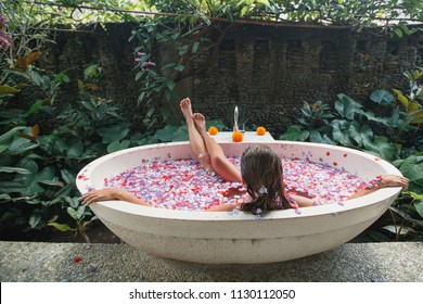 Back View Young Woman Relaxing In Bath With Petals In Tropics. Time For Yourself.