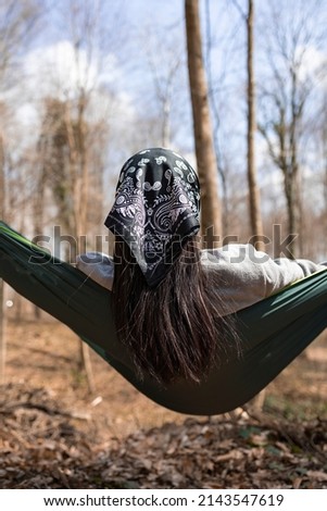 Back view of a young woman relaxing in hammock. Forest background. She has hair band.